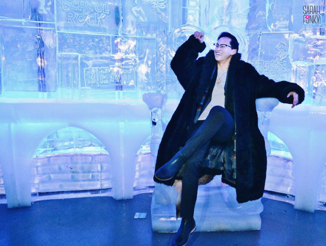 Alex sitting on the ice throne, Broadway show logos carved into the ice wall behind