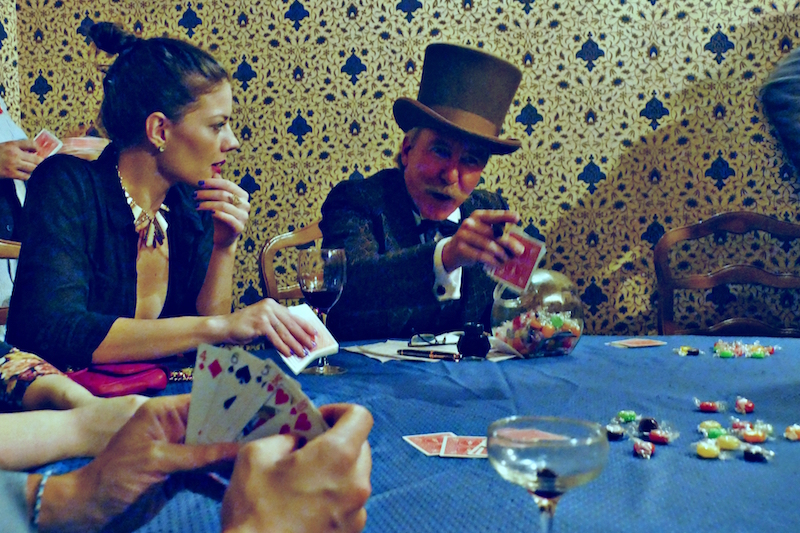 A game of cards unfolds among guests and actors, the line between which frequently blurred
